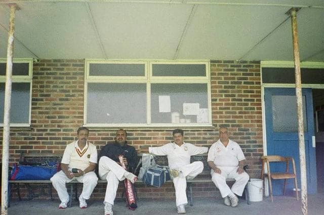 Four players in whites sitting outside a brick pavilion
