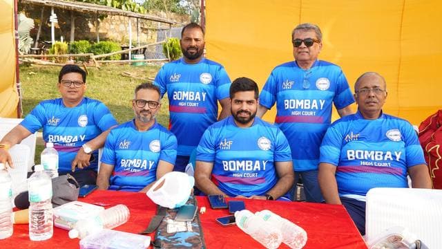 Five players in blue Bombay shirts seated at a table under a tent