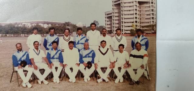 A team in whites and blue sweaters seated in rows in an old photograph