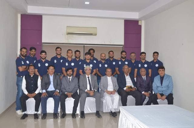 A team in navy shirts standing behind seated men in suits in a hall