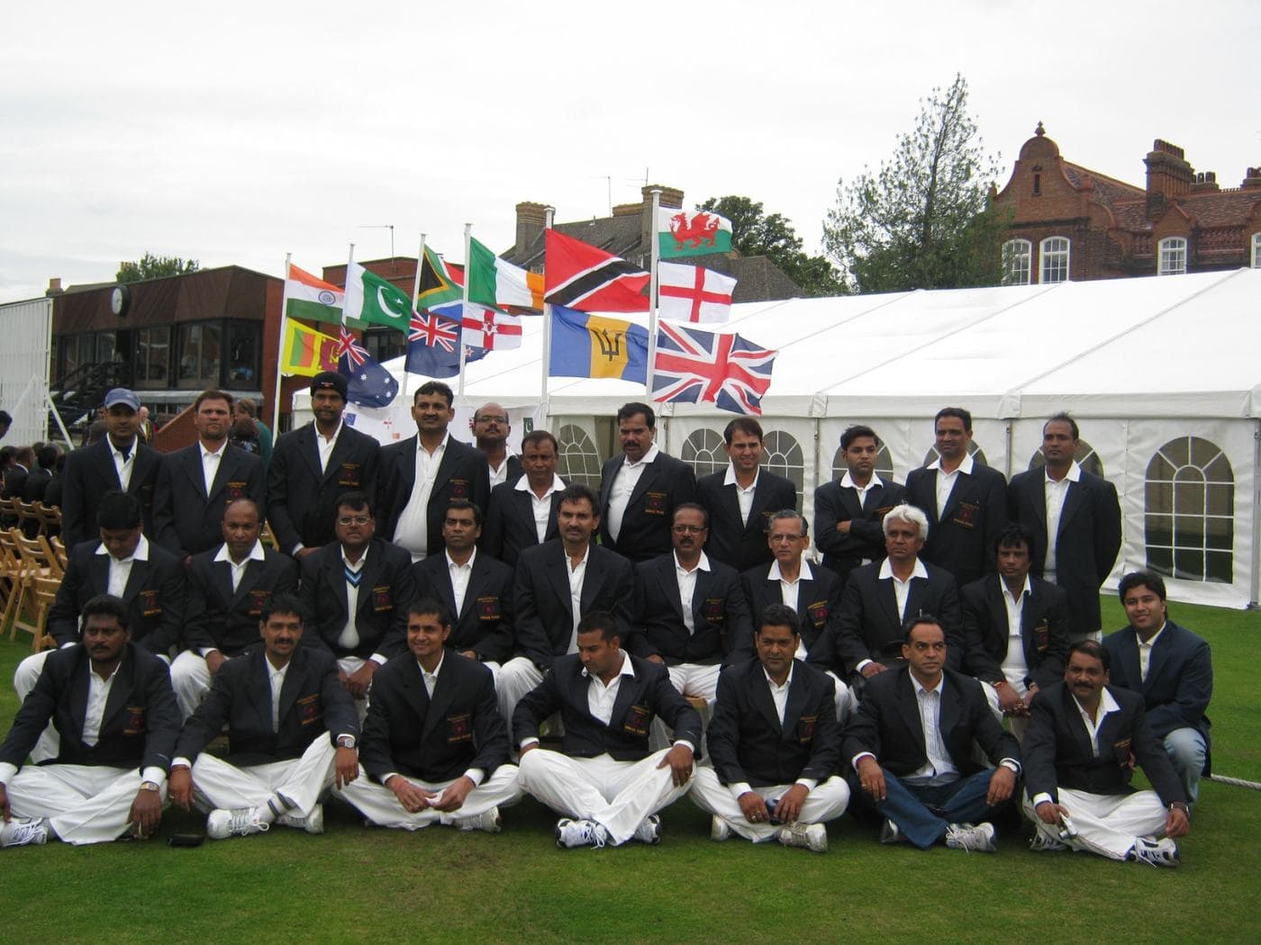A team in blazers and white trousers in front of flags and a marquee