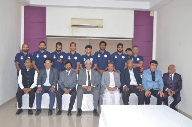 Players standing behind a row of seated officials in a hall
